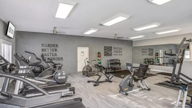 Spacious, well-lit gym featuring treadmills, ellipticals, stationary bikes, weights, and motivational wall text.