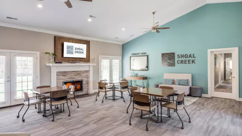 Photograph of a bright community lounge with a fireplace, TV, dining tables, and a blue accent wall with "SHOAL CREEK" text.