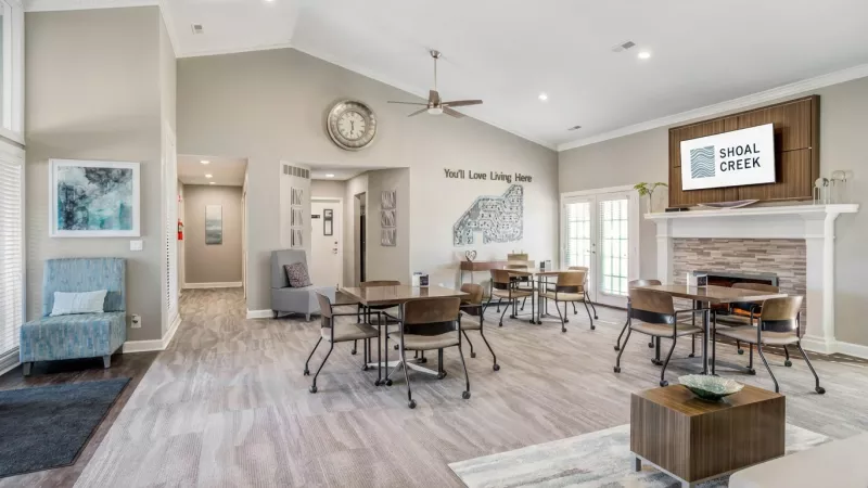 Bright, open community lounge with multiple dining tables, a fireplace, and a light blue armchair.