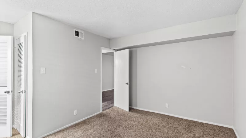Unfurnished bedroom with light gray walls, brown carpet, and two open doorways.