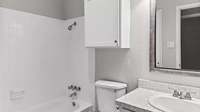 Clean white bathroom with a bathtub, toilet, sink vanity, mirror, and a wall cabinet.