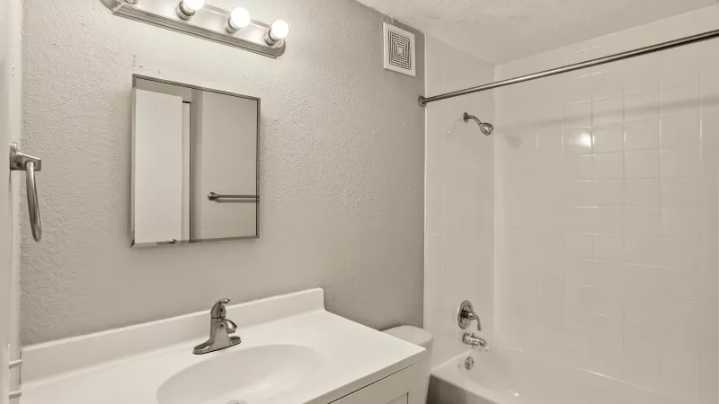 Clean bathroom with white vanity, sink, mirrored medicine cabinet, and toilet. White tub with tiled surround, light gray walls.