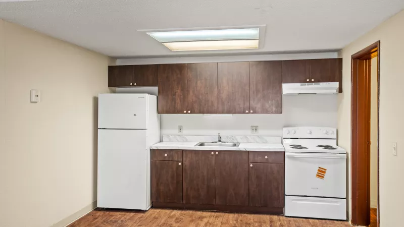 A small kitchen with dark brown cabinets, white refrigerator and stove, and wood-patterned floor.