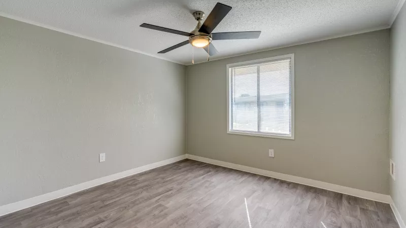 Renovated empty room with light gray-green walls, dark wood-look plank floor, a window, and a ceiling fan.