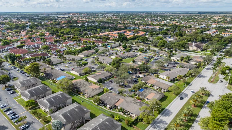 Aerial photograph of a suburban landscape with many houses, green lawns, streets, and trees under a partly cloudy sky.