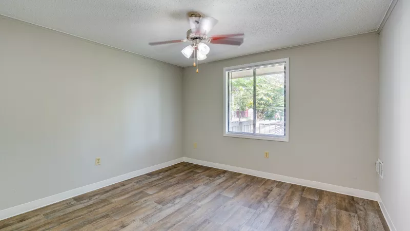 Empty room with light gray walls, wood laminate flooring, a window, and a ceiling fan.