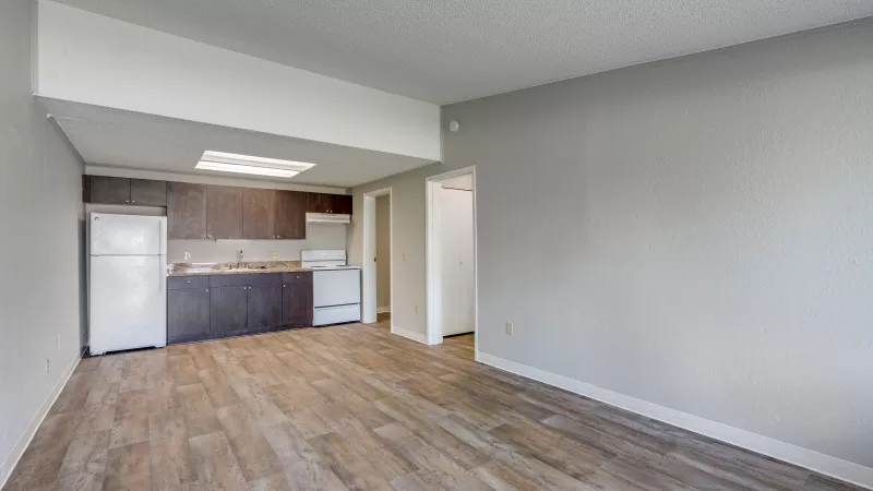 Empty apartment with wood-look flooring and a kitchen featuring dark cabinets and white appliances.
