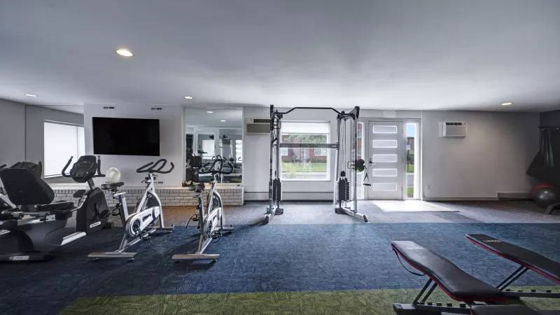 Spacious, well-lit gym with exercise bikes, a multi-station weight machine, and a view of an outdoor green area.