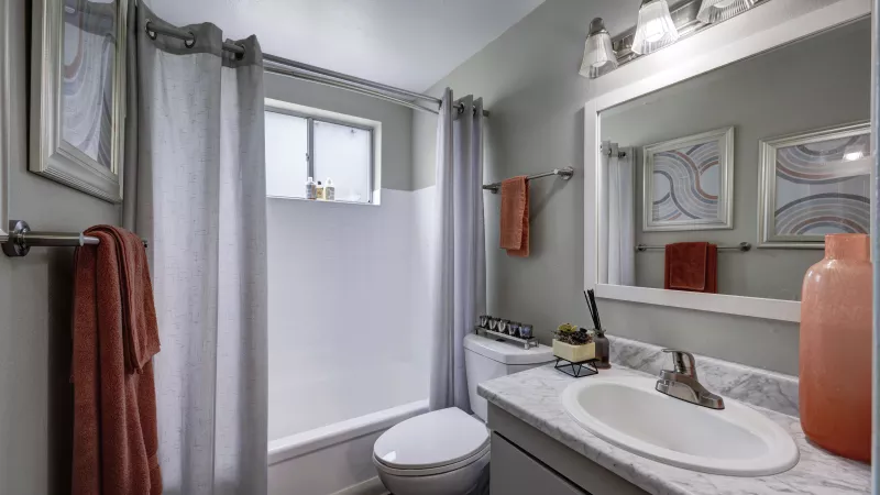 Modern bathroom with gray walls, white tub and vanity. Orange towels and decor add a splash of color.