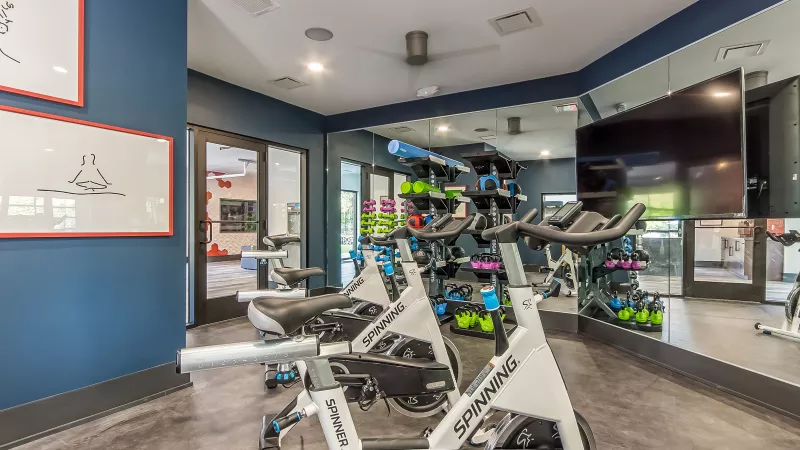 Indoor cycling studio featuring white and blue spin bikes, a mirrored wall with TV, and dark blue accent walls.