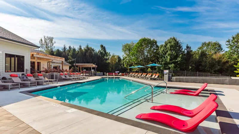 Spacious outdoor swimming pool with turquoise water, red submerged lounge chairs, and poolside seating under a blue sky.