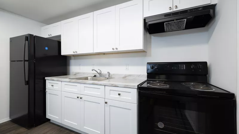 Bright kitchen featuring white cabinets, black refrigerator, electric range, and range hood. Light marble-look counters, dark wood floor.