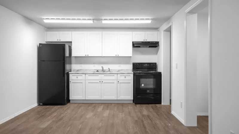 Empty kitchen with white cabinets, black appliances, light wood floor, and white walls.