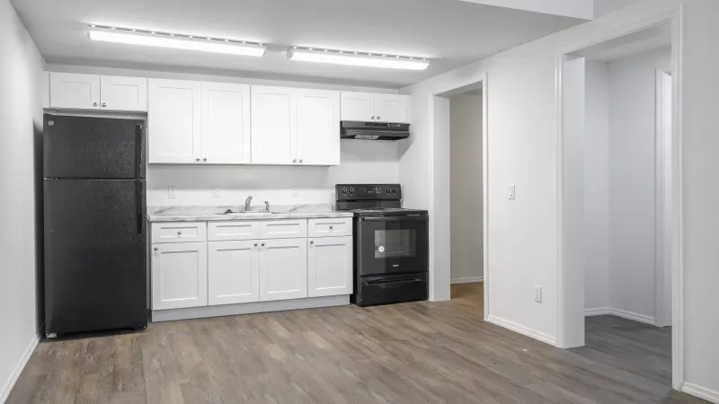Modern kitchen with white cabinets, black appliances, dark counters, wood floor, and overhead lighting.