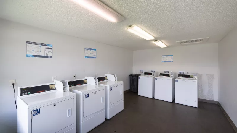 Brightly lit laundromat interior with rows of white washing machines and dryers, white walls, and overhead fluorescent lights.