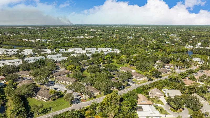 Lush suburban landscape with houses, winding roads, and bodies of water under a bright blue sky.