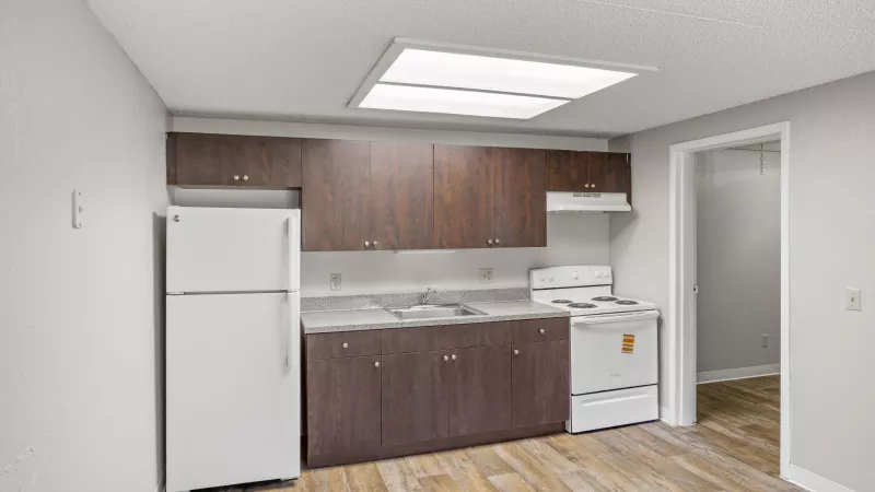 Small kitchen with white refrigerator, range, dark brown cabinets, light gray walls, and wood floor.