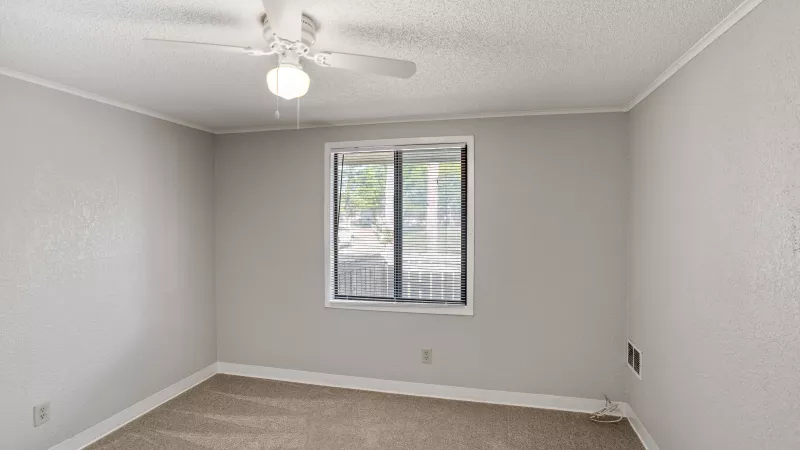 Unfurnished room with light gray walls, beige carpet, a window with blinds, and a white ceiling fan.