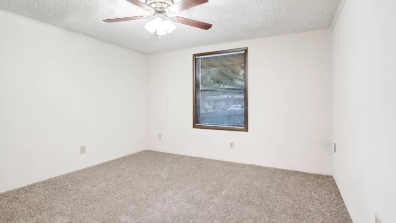 Empty bedroom with light walls, brown carpet, a window, and a ceiling fan.