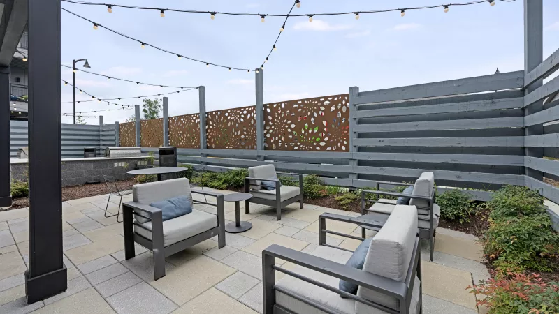 Modern outdoor patio with gray lounge chairs, string lights, paver floor, and a decorative metal privacy screen.