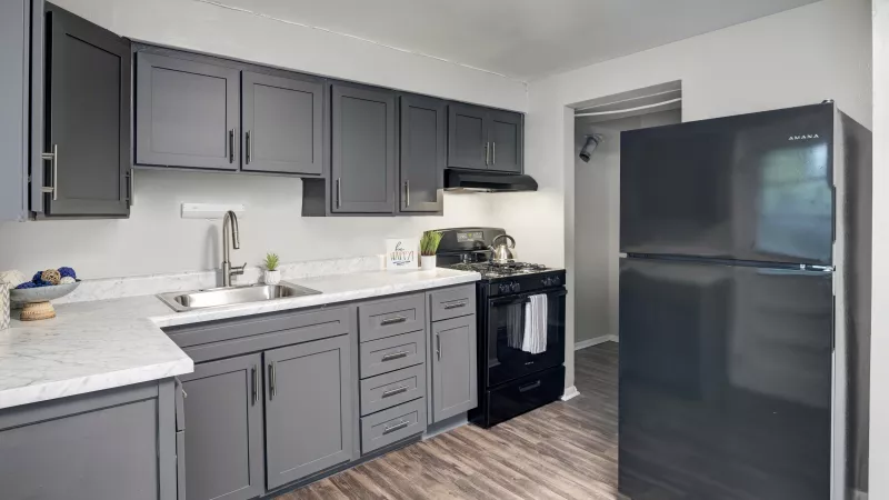 Modern kitchen with dark gray cabinets, white speckled countertops, stainless sink, black stove, black refrigerator, and wood-look floor.