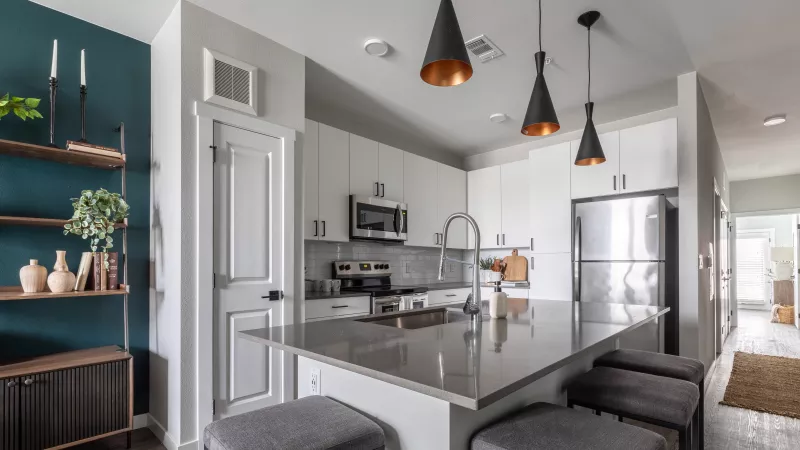 Modern kitchen with white cabinets, stainless steel appliances, a grey island, and a dark teal accent wall.