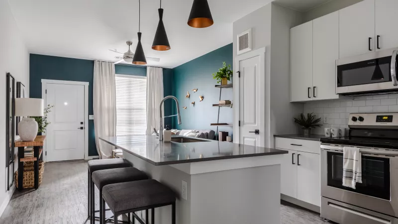 Modern kitchen with white cabinets, stainless steel appliances, a dark island, and a teal accent wall.