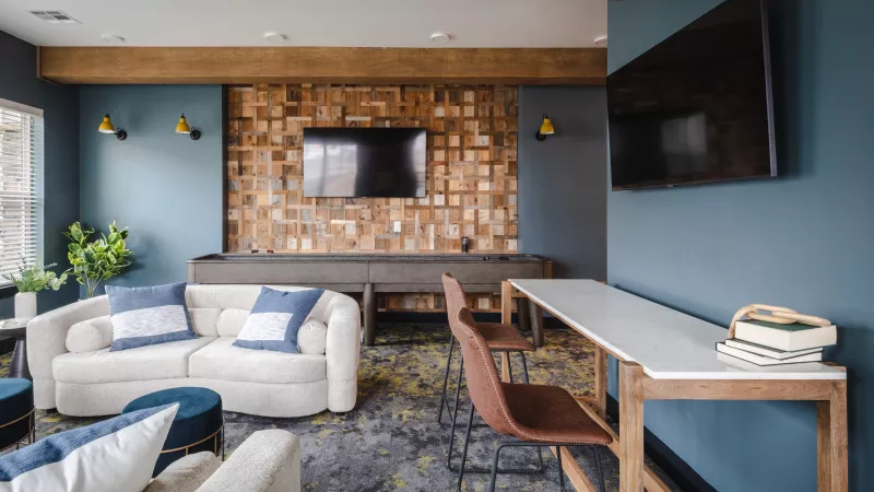 Modern lounge with white sofa, blue walls, a wooden accent wall with a TV, bar table, and patterned rug.
