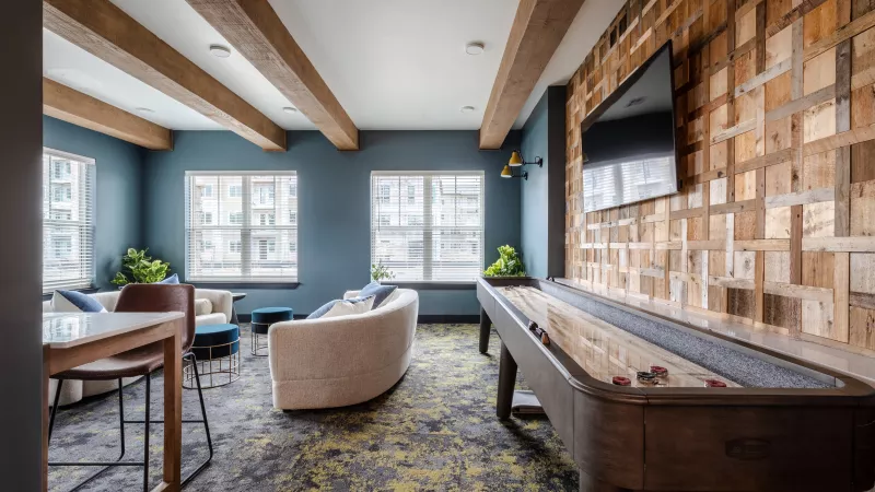 Modern lounge with a shuffleboard table, TV on a textured wood wall, blue walls, and a curved white sofa.