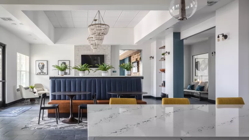 Modern lounge space with a white speckled counter, blue banquette seating, and crystal chandeliers.