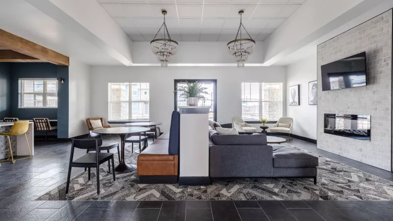 Spacious, modern common lounge with a gray sofa, dark tables, chandeliers, and a fireplace.