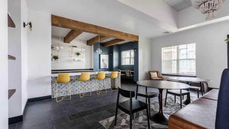Stylish lounge featuring a bar with yellow stools, patterned counter, and multiple seating areas with tables and a sofa.