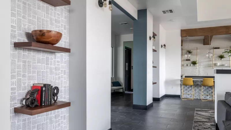 Modern hallway with dark gray tiled floor, white patterned wallpaper, and floating shelves. Teal wall accent in the distance.