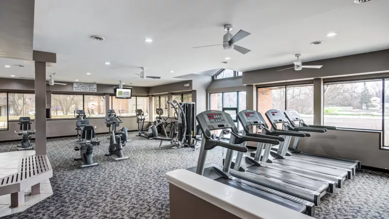 Modern gym with multiple treadmills, exercise bikes, and weight machines. Large windows offer an outdoor view.