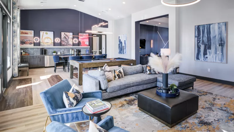 Stylish, modern lounge featuring blue armchairs, a gray sectional sofa, pool table, and a bar area with colorful art.