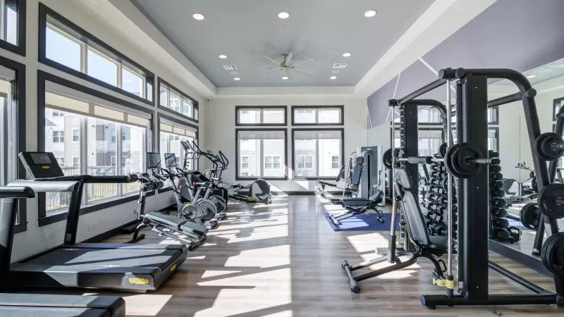 Modern, brightly lit fitness center with multiple treadmills, ellipticals, weight machines, and large windows.