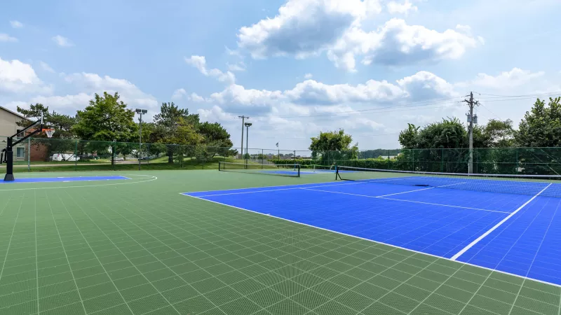 Outdoor green and blue sports courts with trees under a partly cloudy sky.