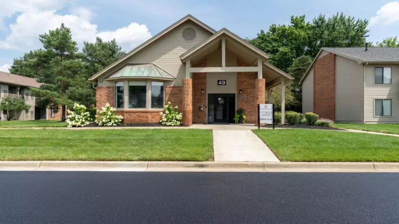 Front exterior of a single-story building with brick and tan siding, a central arched entrance, and a green lawn.