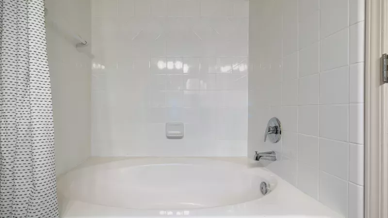White built-in bathtub in a tiled bathroom, with a shower curtain and chrome fixtures.
