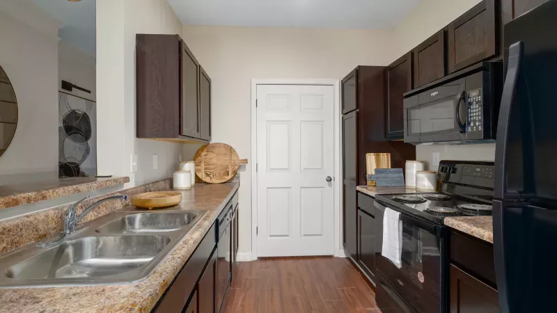 Modern kitchen with dark brown cabinets, speckled countertops, black appliances, a double sink, and wood floors.