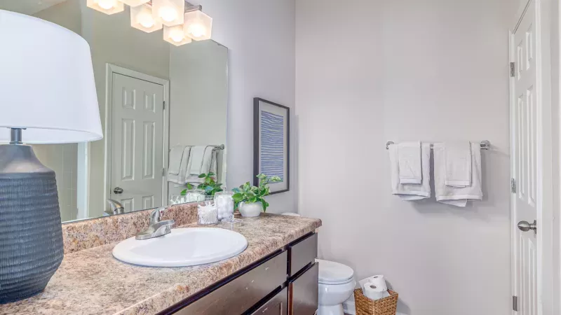 Bright bathroom with a long dark wood vanity, speckled brown countertop, white sink, large mirror, and folded towels.