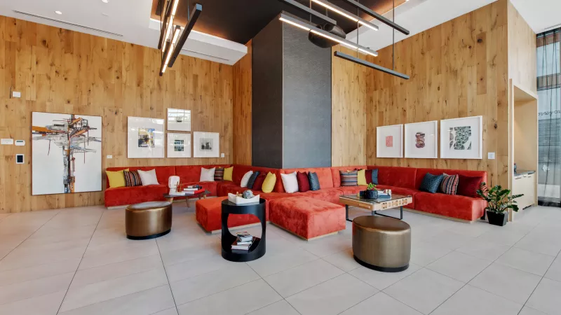 Modern lounge with a large red sectional sofa, colorful pillows, wood walls, abstract art, and stylish coffee tables.