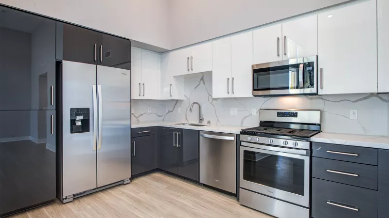 Modern kitchen with dark grey lower and white upper glossy cabinets, stainless steel appliances, and veined white countertops.