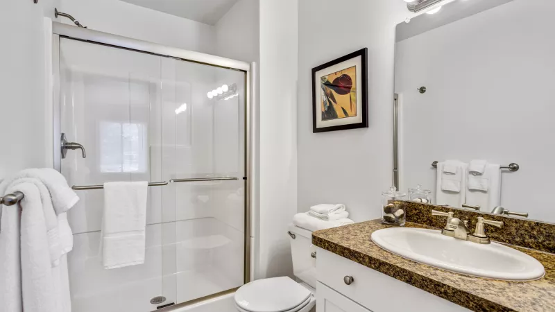 Clean bathroom with a glass shower, white toilet, vanity with a speckled granite countertop, and framed art.