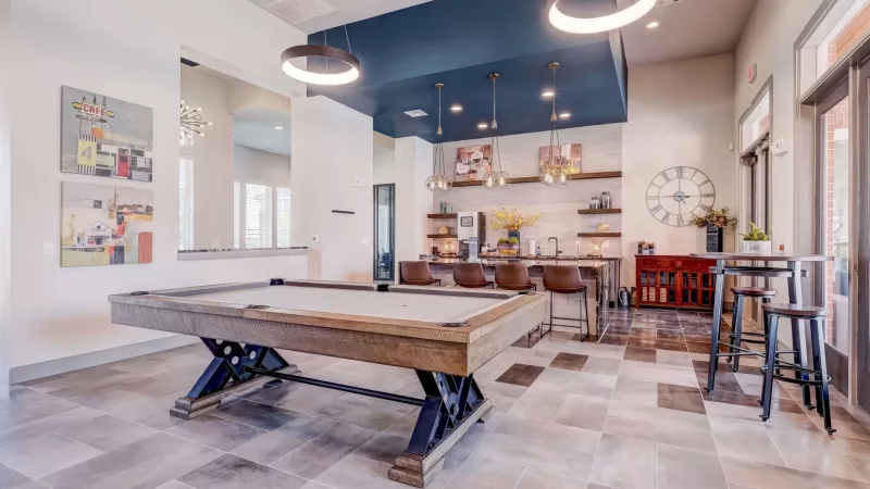 Spacious common room featuring a wooden pool table, a modern bar area with dark blue ceiling, and high-top seating.