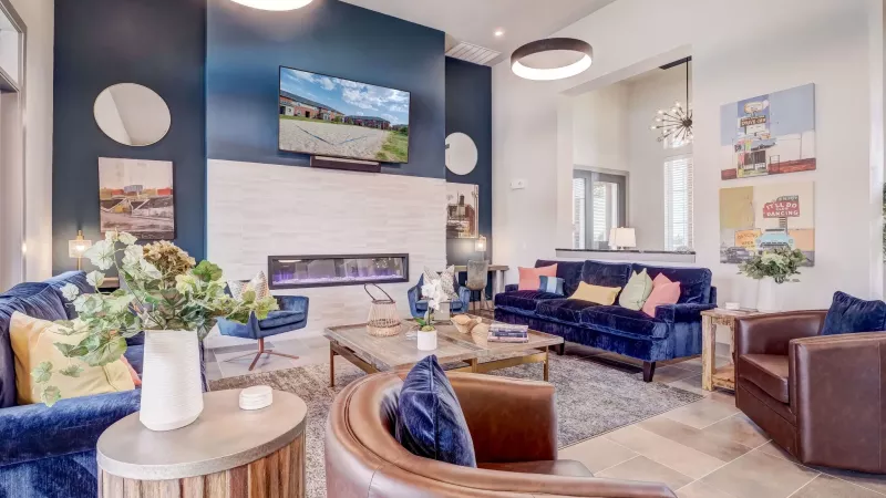 Stylish lounge with blue velvet couches, brown leather armchairs, a white brick fireplace, and a dark blue accent wall.