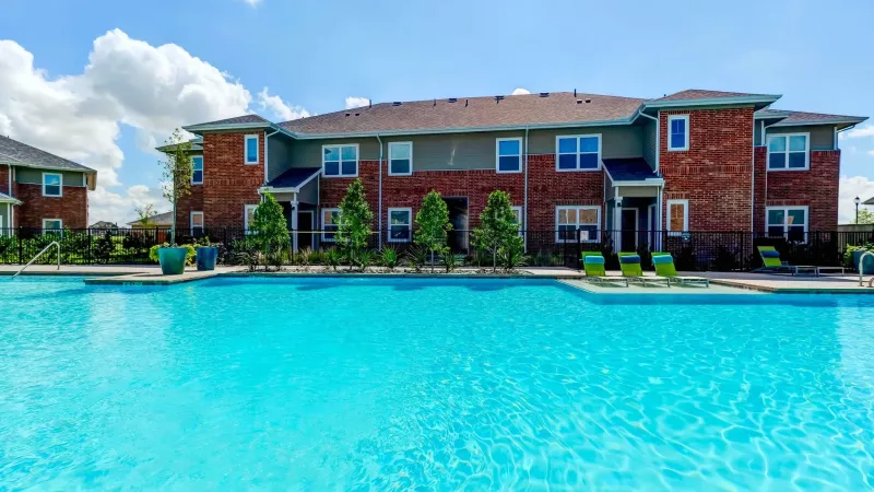 Bright blue swimming pool in front of a modern apartment building with brick facade and balconies under a clear sky.