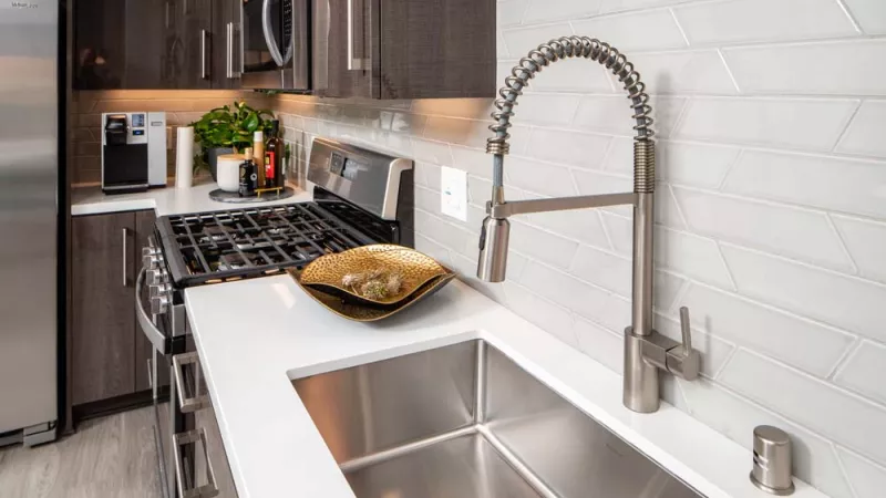 Sleek kitchen with a stainless steel sink, coiled faucet, white counter, dark cabinets, and white chevron tile backsplash.