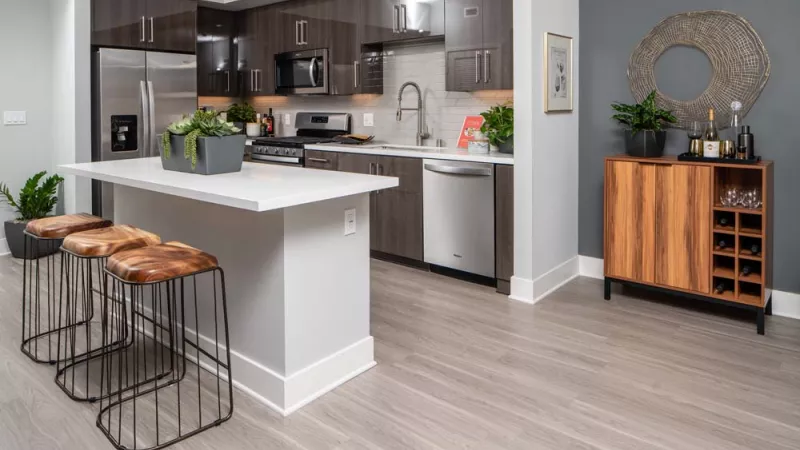 Modern kitchen with dark wood cabinets, stainless steel appliances, a light island with bar stools, and a wooden wine cabinet.
