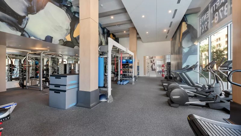 Modern, spacious gym with treadmills, ellipticals, weight machines, and large abstract art on the walls.